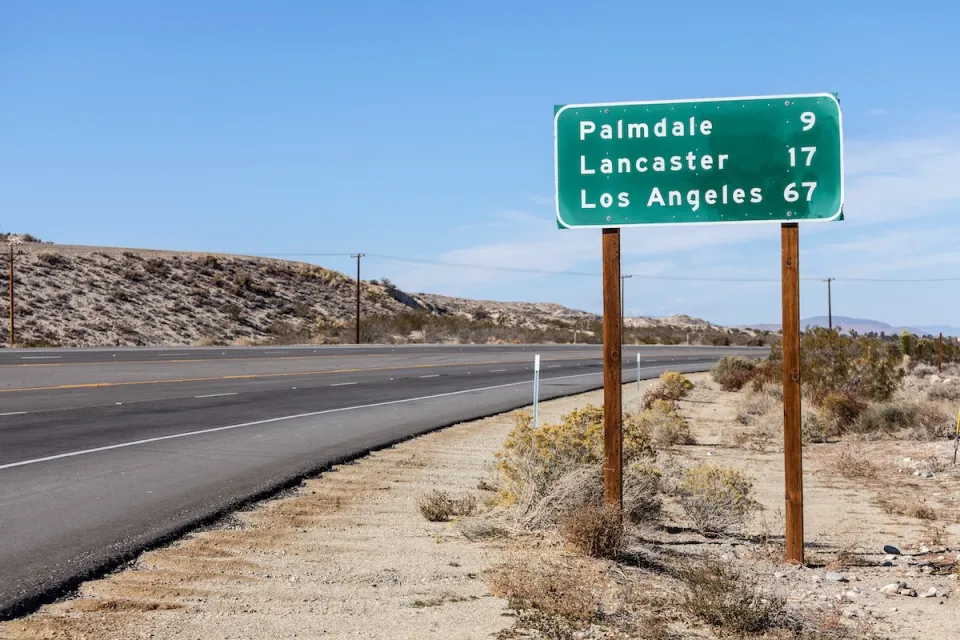 Green highway sign with white text with distances for Palmdale, Lancaster, and Los Angeles, California.